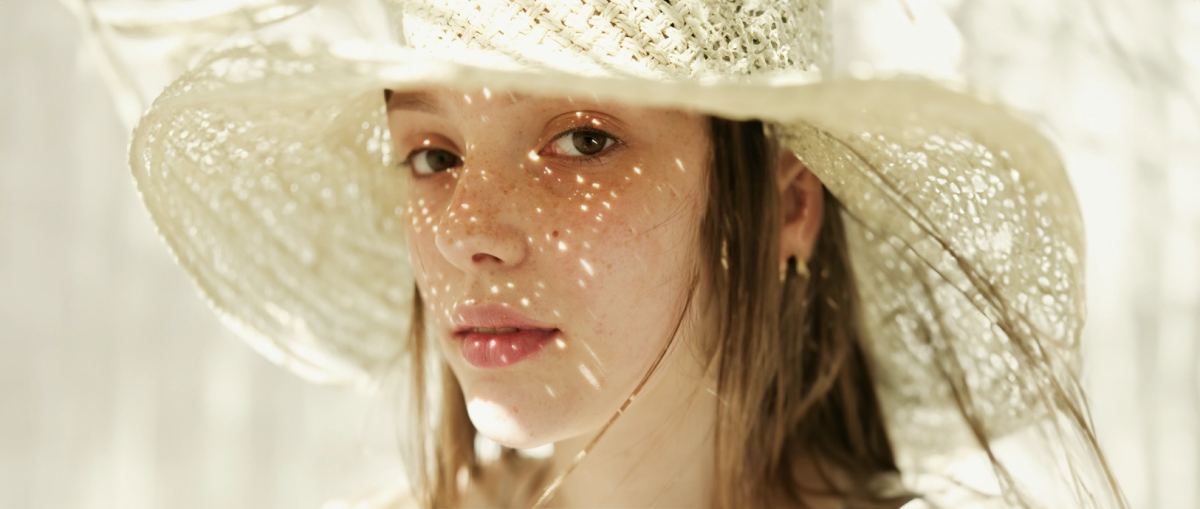 Vrouw met hoed op en zonnestralen op haar gezicht.