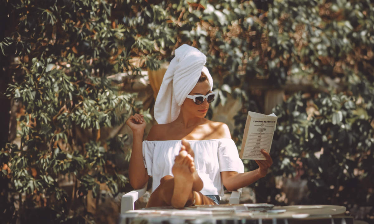 Vrouw met handdoek op haar hoofd leest boek buiten in de zon.